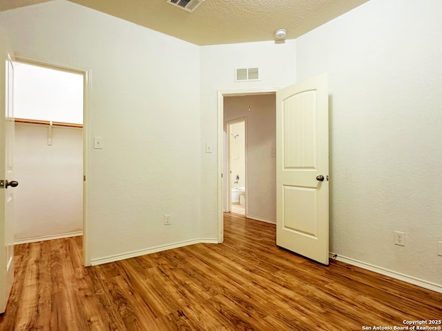 unfurnished bedroom with hardwood / wood-style flooring, a walk in closet, a textured ceiling, and a closet