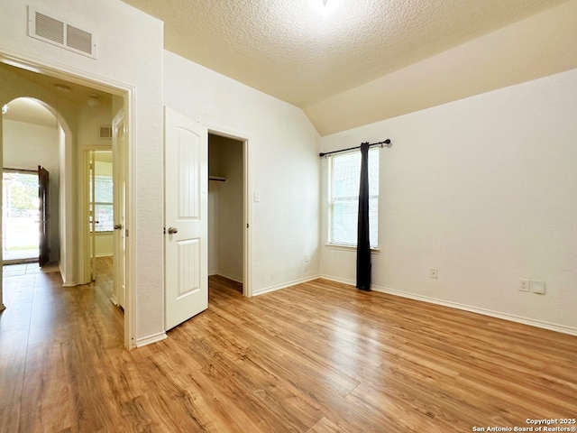 unfurnished bedroom featuring a walk in closet, vaulted ceiling, a textured ceiling, and light wood-type flooring