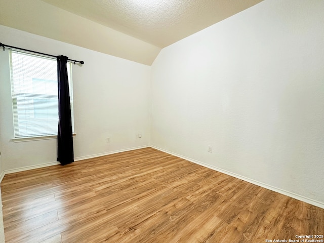 empty room with vaulted ceiling, a textured ceiling, and light hardwood / wood-style floors