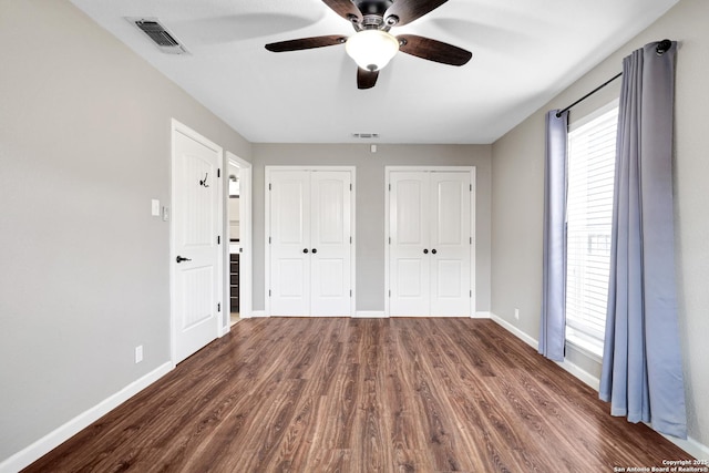 unfurnished bedroom featuring two closets, dark hardwood / wood-style floors, and ceiling fan