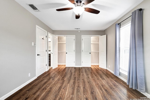 unfurnished bedroom with dark wood-type flooring, ceiling fan, and two closets