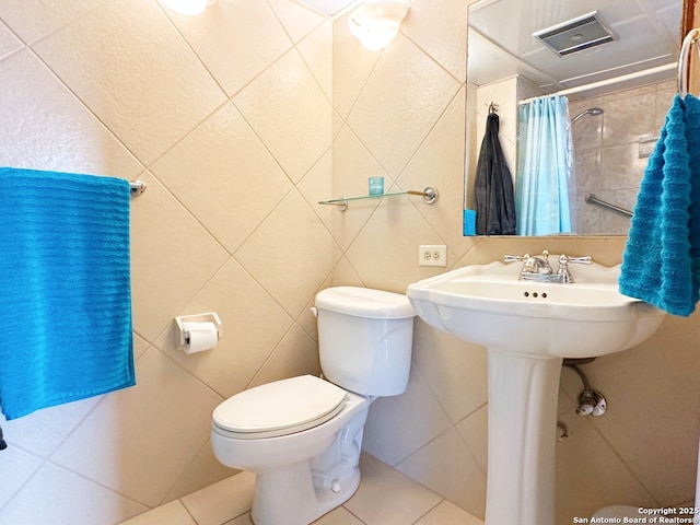 bathroom featuring toilet, curtained shower, tile patterned flooring, and tile walls