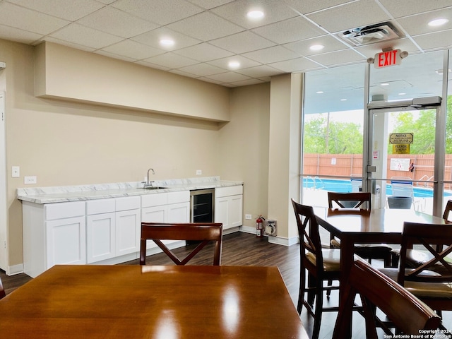 interior space with dark wood-type flooring, a paneled ceiling, indoor wet bar, floor to ceiling windows, and wine cooler