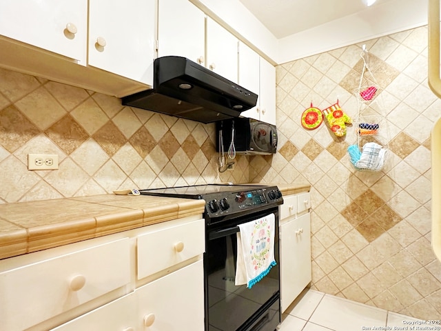 kitchen featuring light tile patterned flooring, range hood, white cabinetry, tile counters, and black appliances