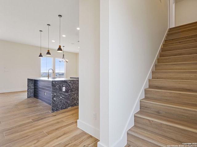 stairs with wood-type flooring, sink, and an inviting chandelier