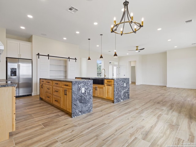 kitchen with stone counters, hanging light fixtures, a spacious island, stainless steel fridge with ice dispenser, and a barn door