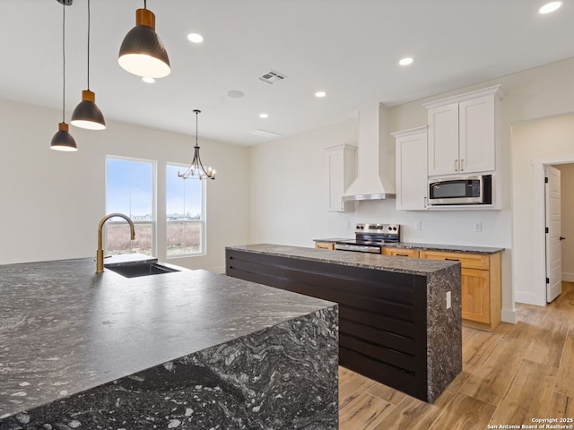 kitchen featuring sink, white cabinets, stainless steel appliances, a center island with sink, and wall chimney range hood