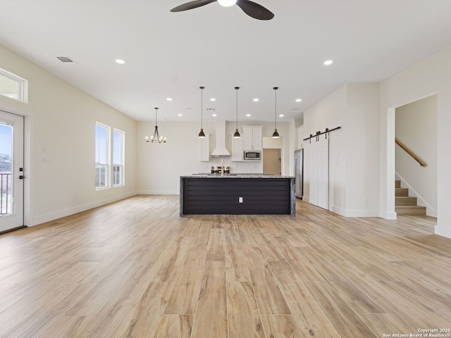 unfurnished living room with a barn door, ceiling fan with notable chandelier, and light wood-type flooring