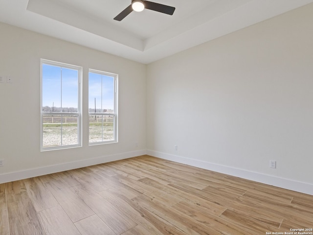 empty room featuring a raised ceiling, ceiling fan, and light hardwood / wood-style floors