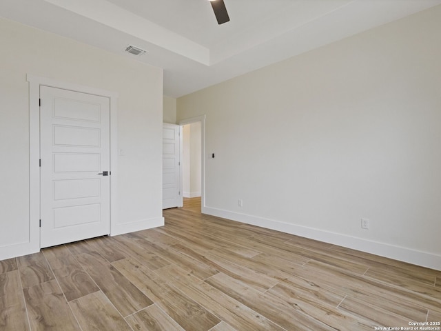 unfurnished bedroom with ceiling fan, light wood-type flooring, and a tray ceiling