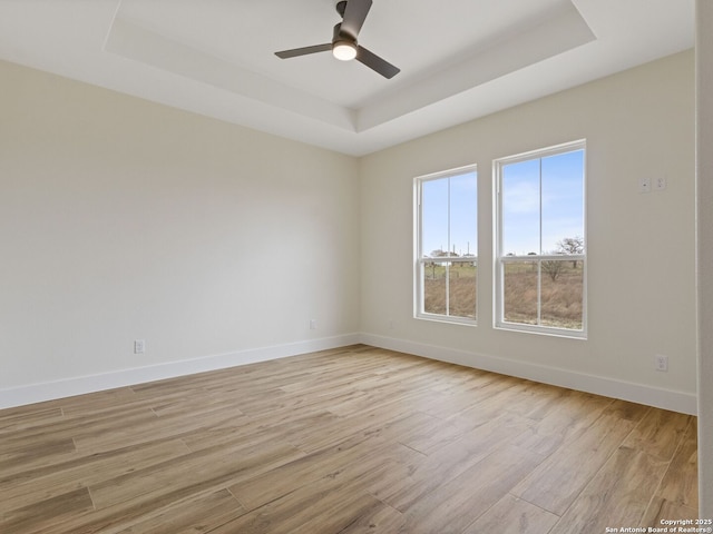 unfurnished room with a raised ceiling, ceiling fan, and light hardwood / wood-style floors