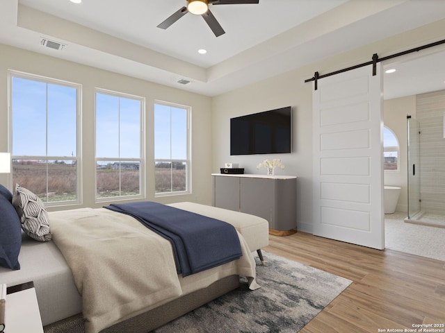 bedroom featuring ceiling fan, a barn door, light hardwood / wood-style floors, and a tray ceiling