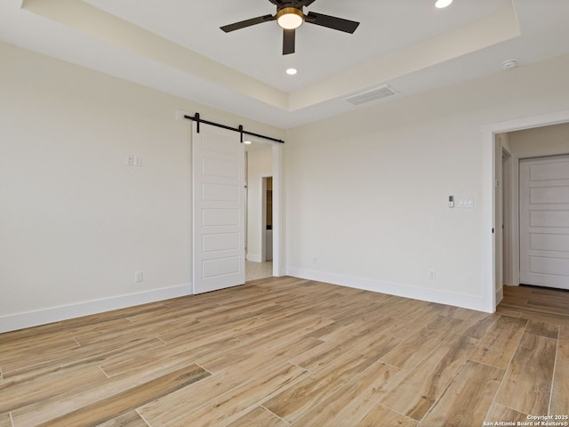 spare room featuring a raised ceiling, ceiling fan, a barn door, and light wood-type flooring