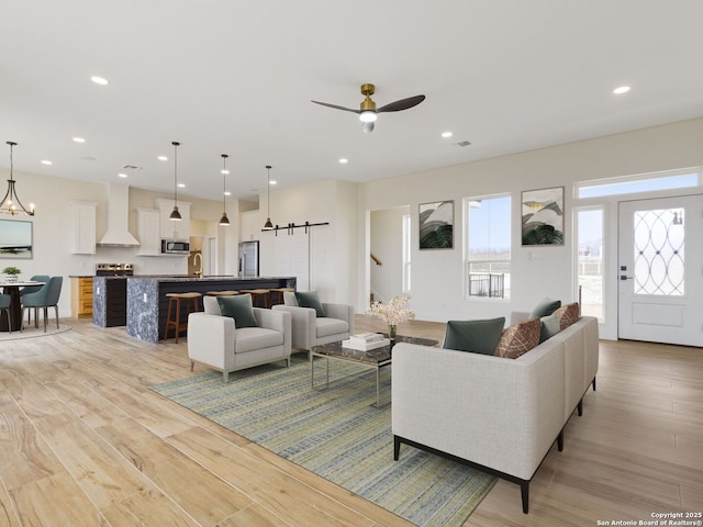 living room with sink, light hardwood / wood-style floors, a barn door, and ceiling fan