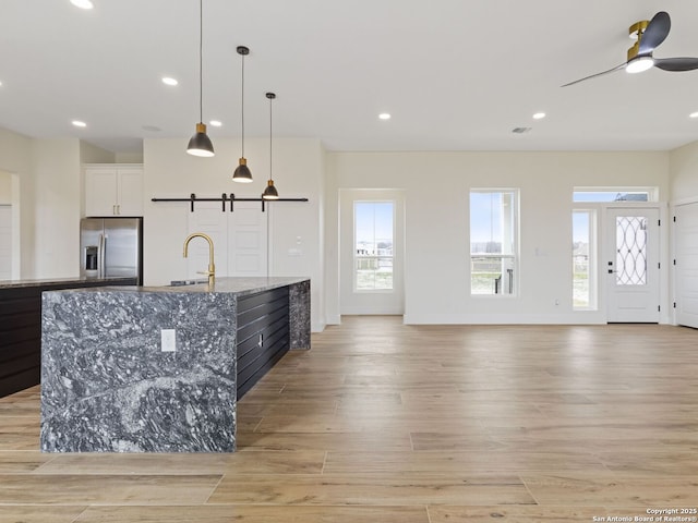 kitchen with sink, white cabinets, stainless steel refrigerator with ice dispenser, light stone countertops, and a spacious island