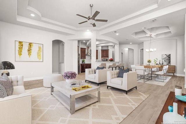 living room with a raised ceiling, ceiling fan with notable chandelier, and light wood-type flooring