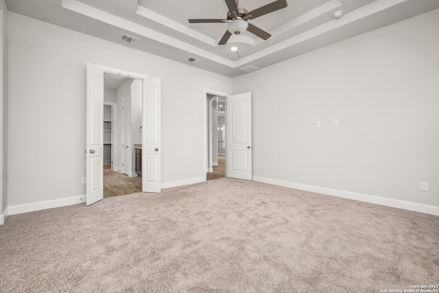 unfurnished bedroom featuring a raised ceiling, ceiling fan, carpet, and ensuite bath