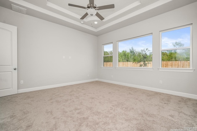 empty room with a raised ceiling, ceiling fan, and carpet flooring