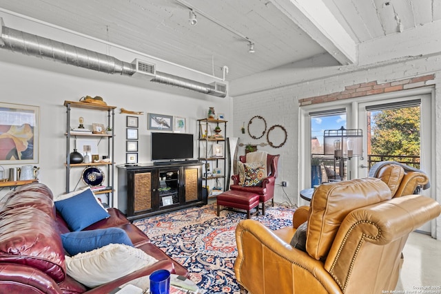 living room featuring beamed ceiling, brick wall, and track lighting