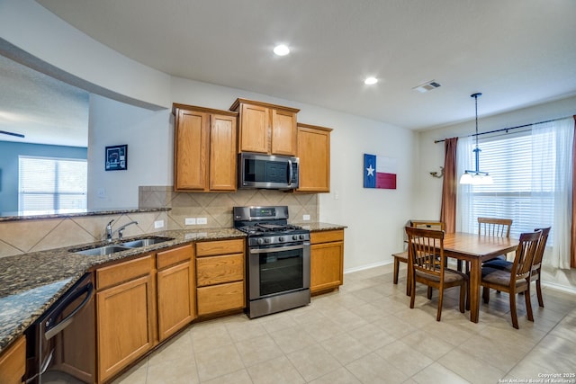 kitchen with sink, appliances with stainless steel finishes, dark stone countertops, hanging light fixtures, and tasteful backsplash