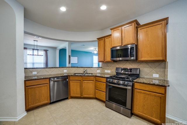 kitchen with tasteful backsplash, sink, dark stone counters, hanging light fixtures, and stainless steel appliances