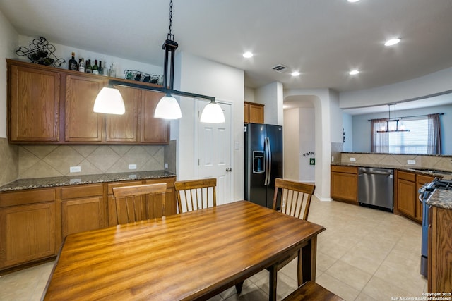 kitchen with stainless steel appliances, tasteful backsplash, dark stone countertops, and decorative light fixtures