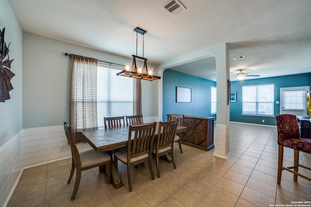 tiled dining space with ceiling fan with notable chandelier and a textured ceiling