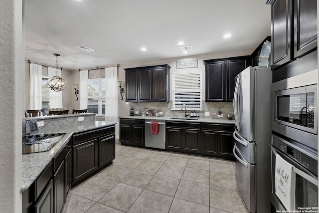 kitchen with sink, backsplash, hanging light fixtures, light stone counters, and stainless steel appliances