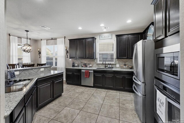 kitchen featuring pendant lighting, sink, decorative backsplash, stainless steel appliances, and light stone countertops