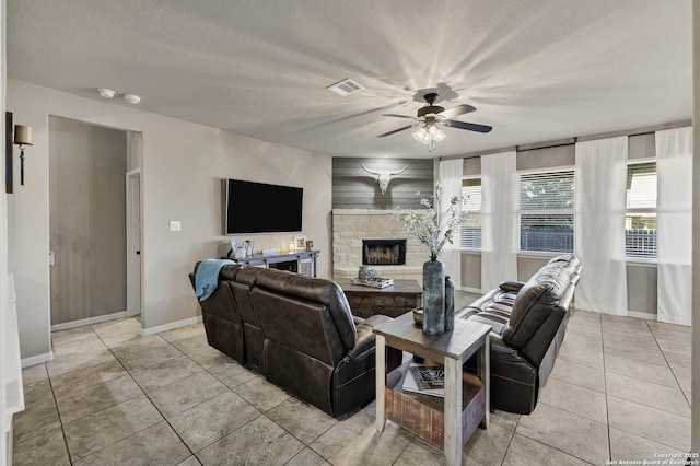 tiled living room featuring ceiling fan, a fireplace, and a textured ceiling