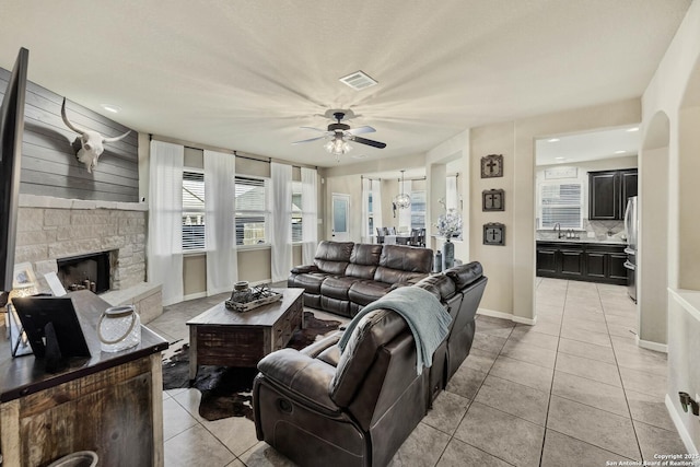 tiled living room with ceiling fan, sink, and a fireplace