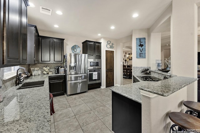 kitchen with sink, a kitchen breakfast bar, kitchen peninsula, stainless steel appliances, and light stone countertops