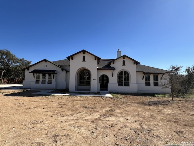 mediterranean / spanish house featuring a shingled roof, a chimney, and stucco siding