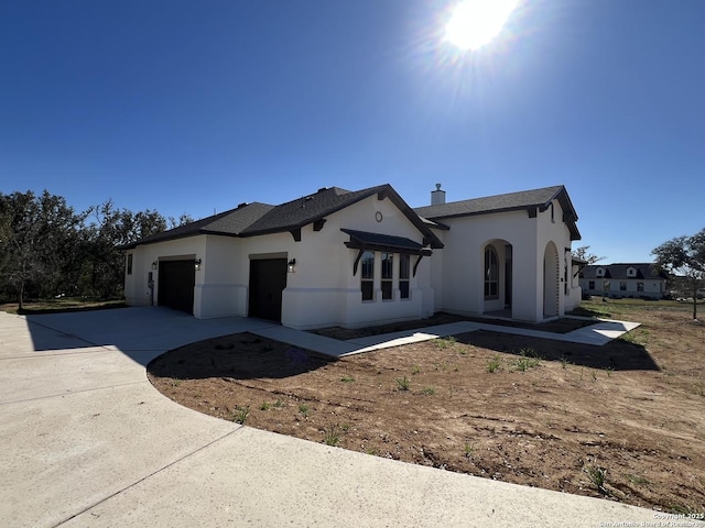 view of front of property featuring an attached garage, a chimney, concrete driveway, and stucco siding