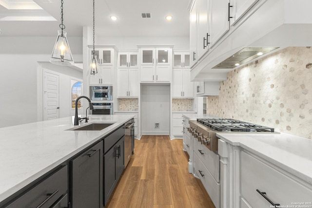 kitchen featuring pendant lighting, glass insert cabinets, white cabinetry, a sink, and dark cabinets