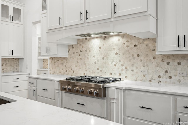 kitchen with stainless steel gas stovetop, decorative backsplash, glass insert cabinets, white cabinetry, and light stone countertops