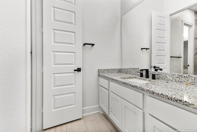 bathroom featuring a textured wall, vanity, and baseboards