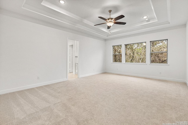 empty room featuring baseboards, a raised ceiling, crown molding, and light colored carpet