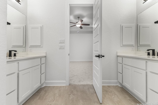 bathroom featuring a ceiling fan, two vanities, and a sink