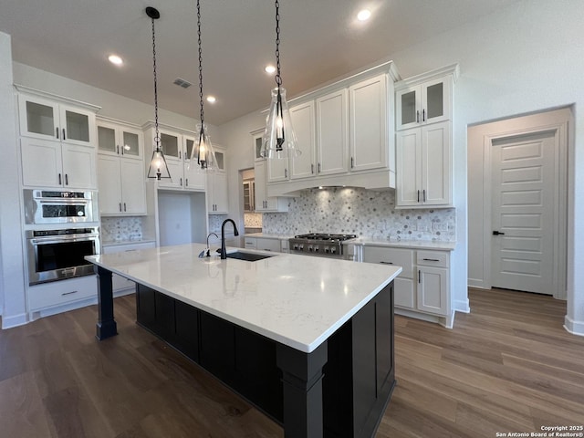 kitchen featuring decorative light fixtures, white cabinetry, a sink, an island with sink, and range