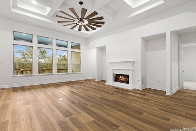 unfurnished living room with coffered ceiling, a lit fireplace, a towering ceiling, and wood finished floors