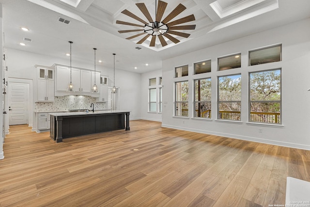 kitchen featuring white cabinets, an island with sink, open floor plan, light countertops, and pendant lighting