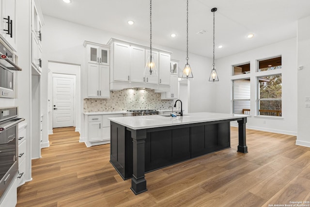 kitchen with a kitchen island with sink, light countertops, glass insert cabinets, and white cabinetry