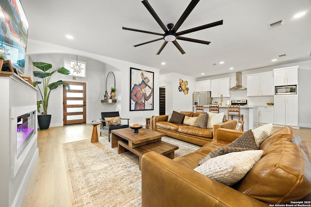 living room with crown molding, sink, ceiling fan, and light wood-type flooring