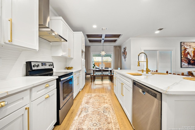 kitchen with wall chimney range hood, sink, a kitchen island with sink, stainless steel appliances, and white cabinets