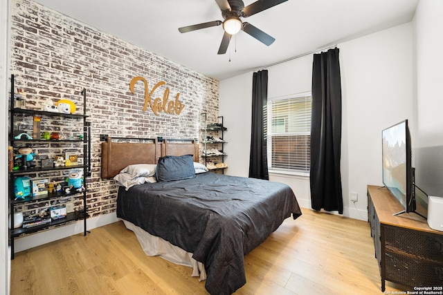 bedroom with light hardwood / wood-style flooring, ceiling fan, and brick wall