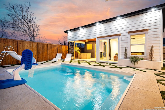 pool at dusk with a water slide and a patio area