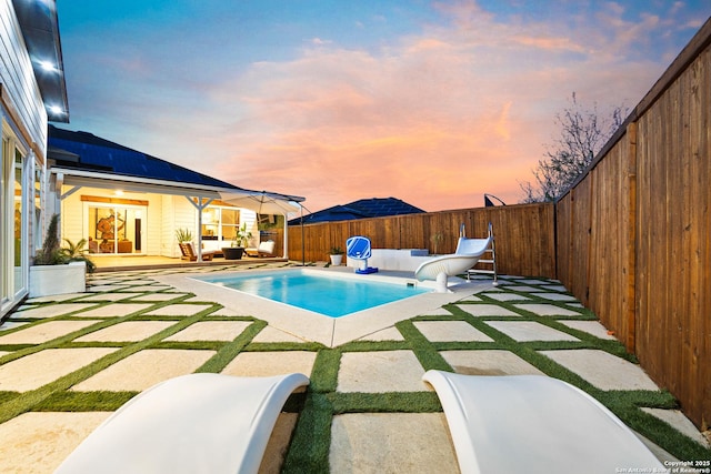 pool at dusk with a water slide, an outdoor hangout area, and a patio area