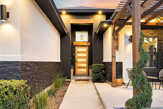 exterior entry at dusk featuring a pergola and a patio area