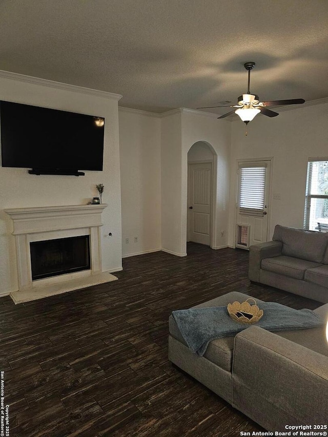 living room with ceiling fan, crown molding, dark wood-type flooring, and a textured ceiling